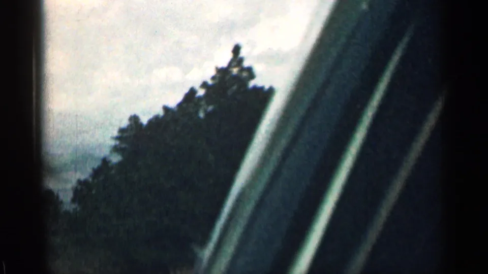 Passenger-side car window frame fills the edge of this 1963 Colorado home-movie frame, with trees and cloudy sky outside.
