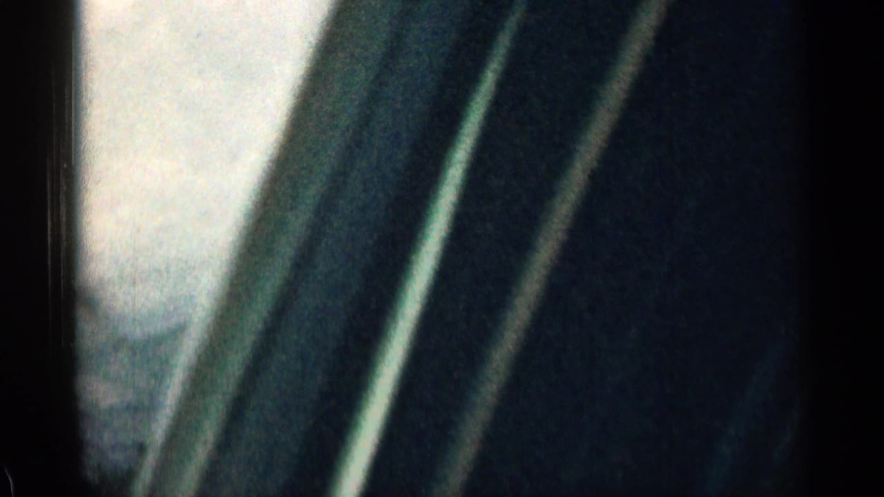 1963 Colorado 8mm frame from inside a moving vehicle, showing dark window framing, soft sky, and blurred roadside scenery.