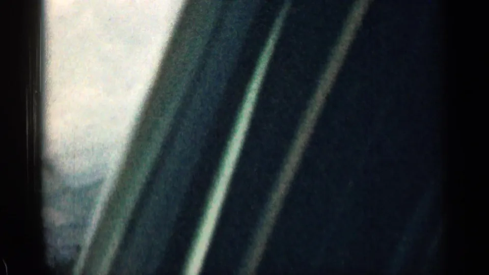 1963 Colorado 8mm frame from inside a moving vehicle, showing dark window framing, soft sky, and blurred roadside scenery.