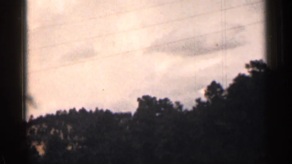 1963 Colorado travel footage showing power lines, wooded hills, pale sky, and the dark border of a moving car-window view.