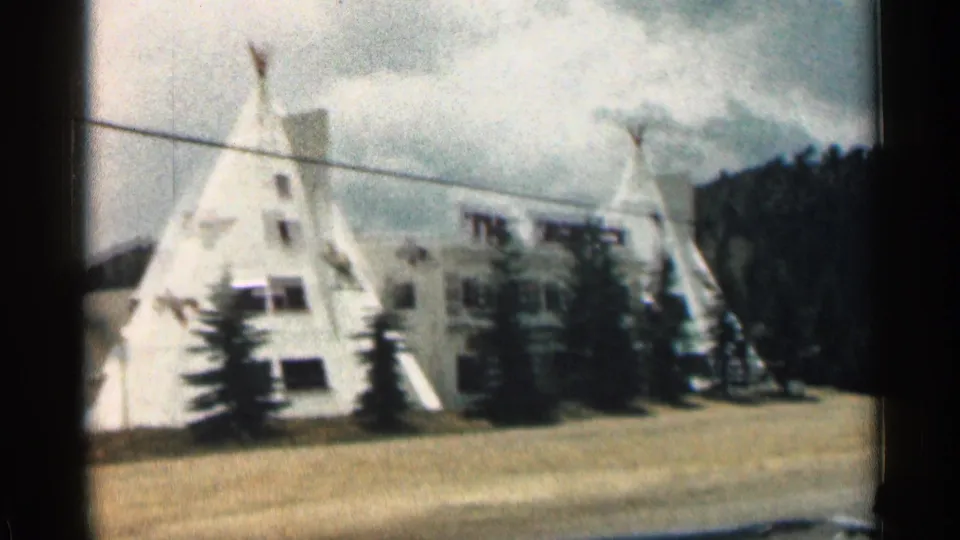 1963 Colorado frame with multiple white teepee-shaped roadside buildings, trees, and a partly obscured THE TEEPEES sign.