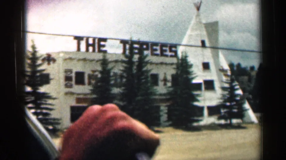 1963 Colorado home-movie frame showing THE TEEPEES sign on a roadside building, flanked by teepee forms and trees.