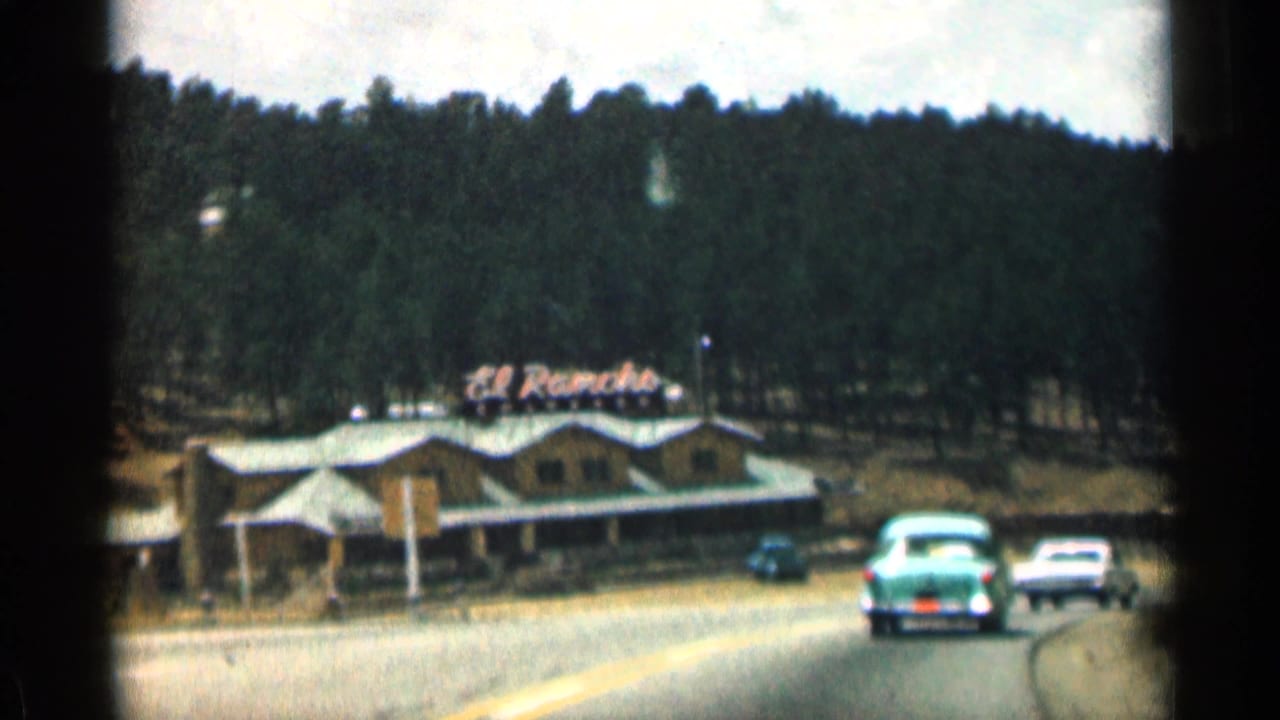 Roadside El Rancho restaurant with classic cars and pine hillside behind it.