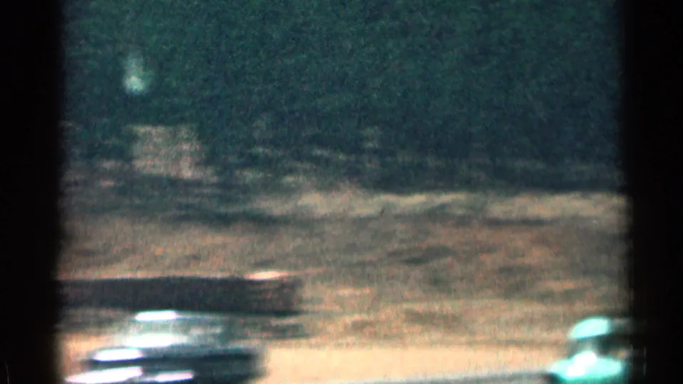 Motion-blurred 1963 Colorado roadside frame showing highway pavement, trees, and a passing classic car from a moving vehicle.