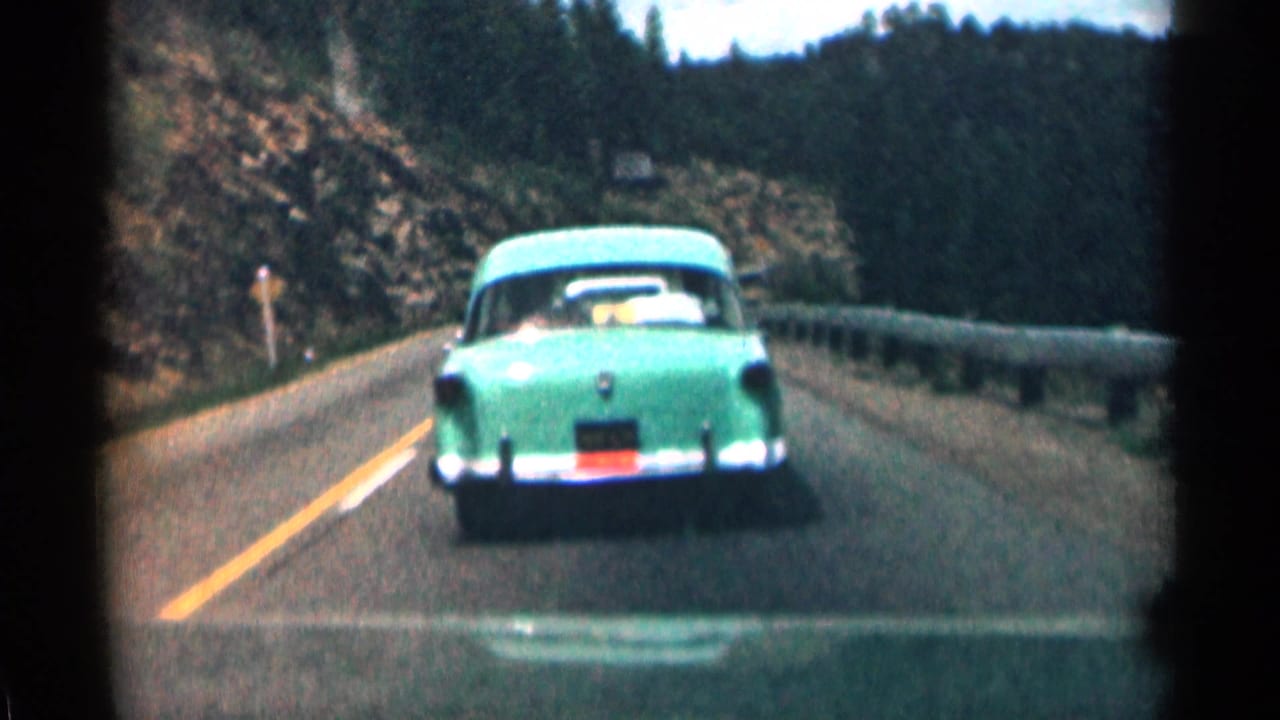 Rear view of a green 1950s sedan on a curving Colorado mountain highway, filmed from a following vehicle.