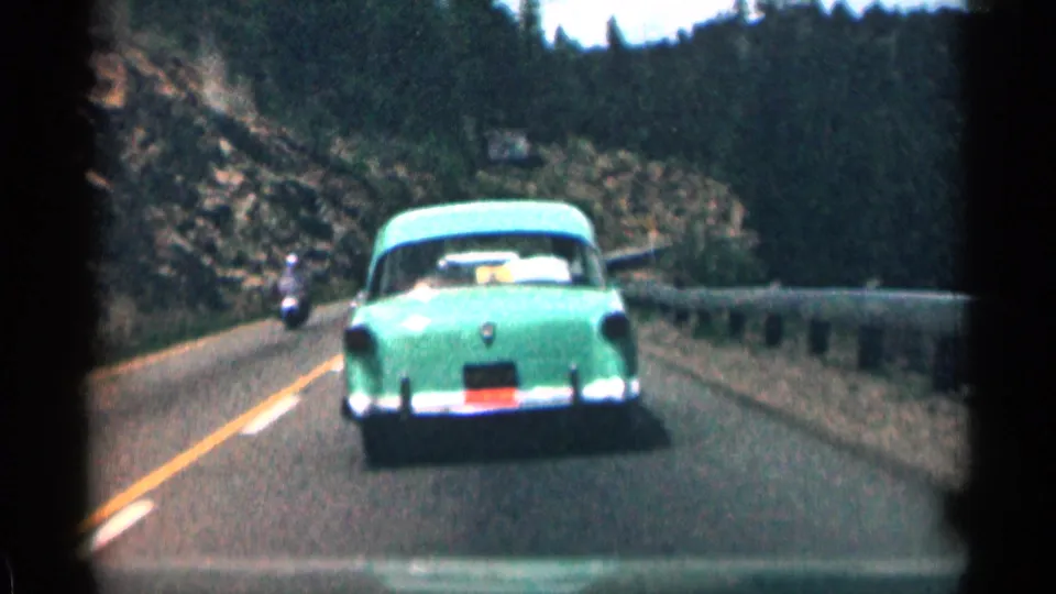 Green sedan on a Colorado mountain road with a small oncoming motorcycle or vehicle visible at the left edge.