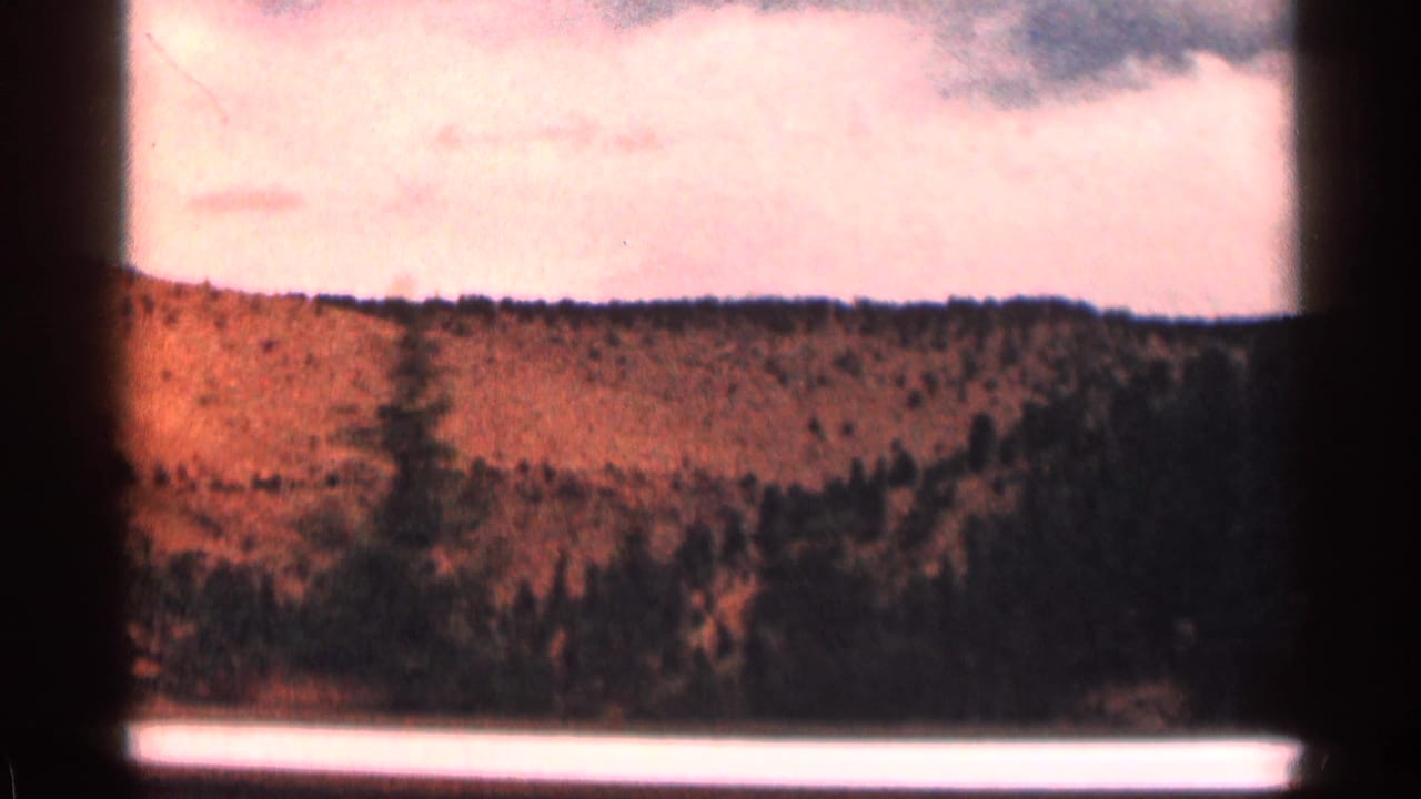 Forested mountain slope and orange hillside seen through a dark 8mm frame border.