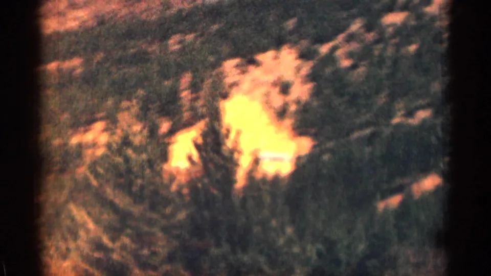 Soft 8mm view of a Colorado mountain slope with trees and a bright sunlit clearing or water area.