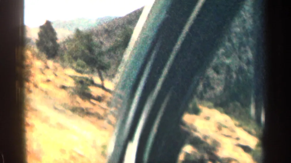 Passenger-side 8mm view from a moving car in Colorado, with the window frame visible beside trees and hills.