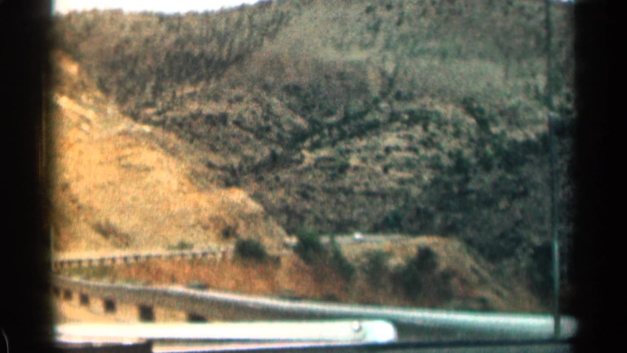 Mountain road and guardrail seen through a car window beside dry Colorado hills.