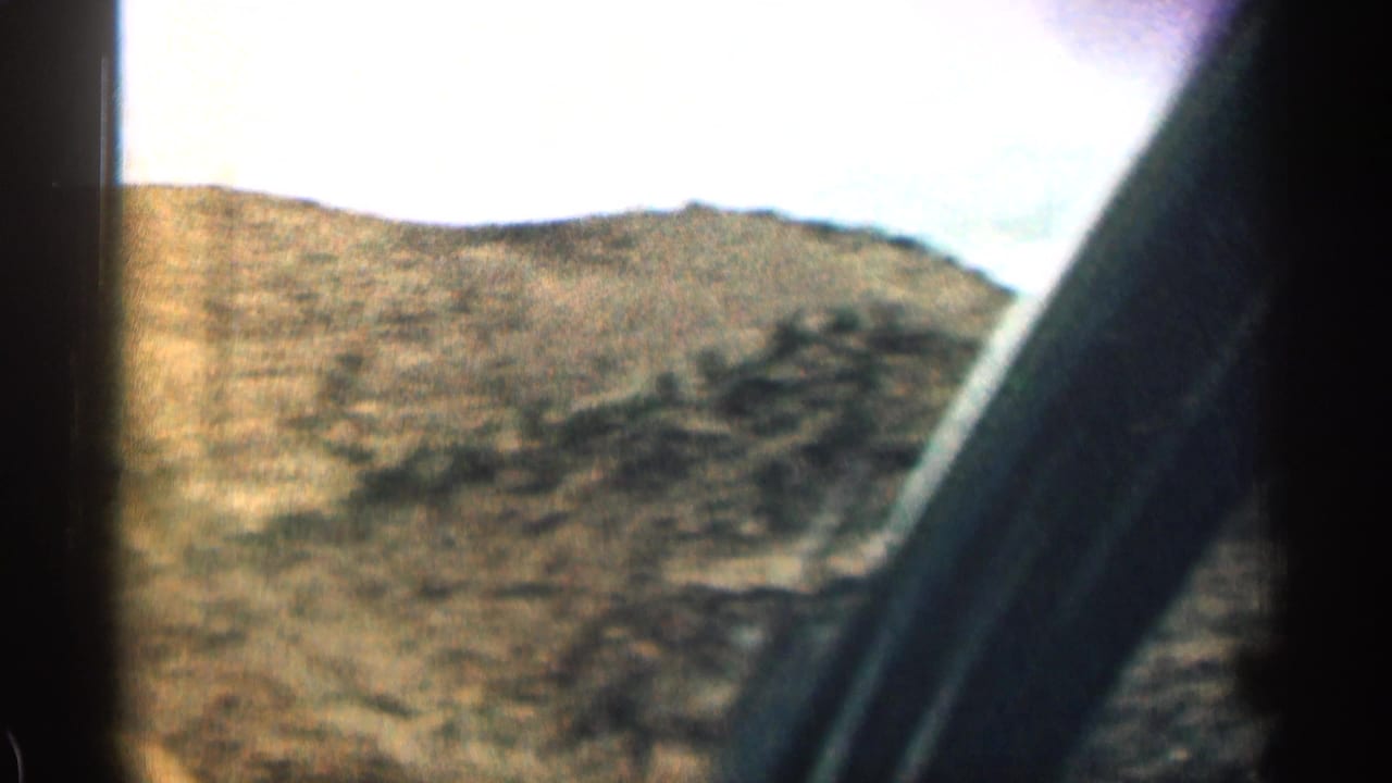 Dry mountain hillside seen past the dark frame of a vehicle window.