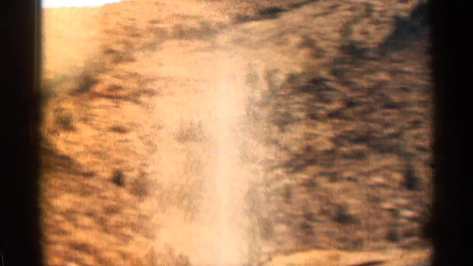 1963 Colorado home-movie frame showing motion-blurred roadside brush and dry slope during a mountain drive.
