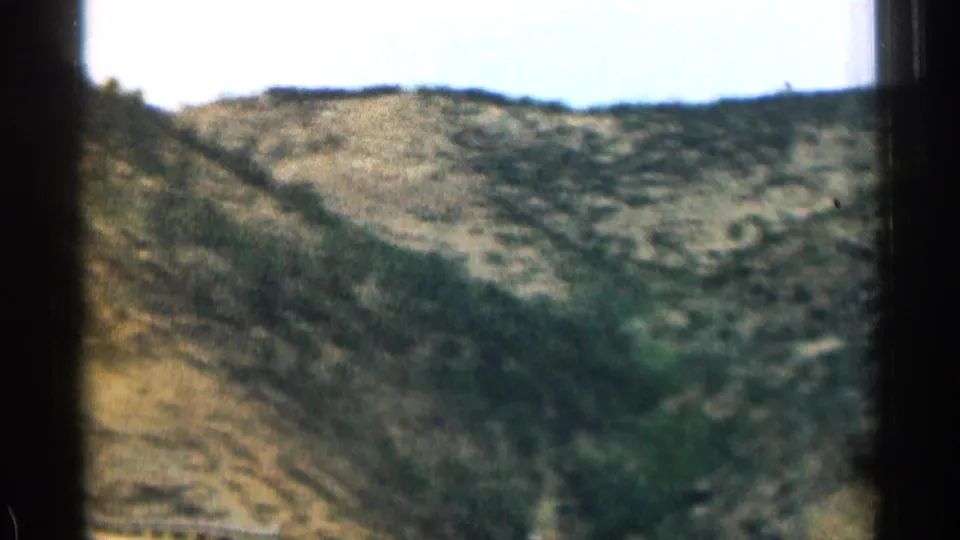 1963 Colorado car-window view of rugged hills, sparse vegetation, and a shallow ravine in soft 8mm color.