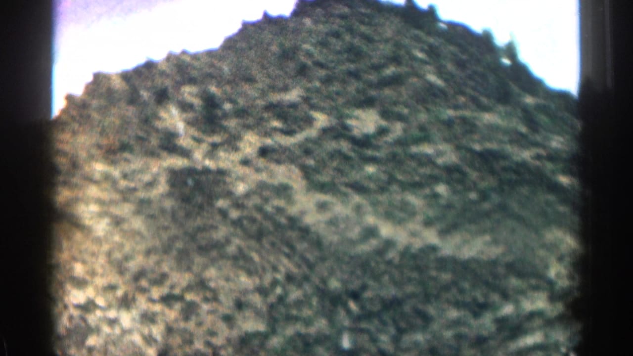 Close view of a rocky scrub-covered hill beneath a bright sky.