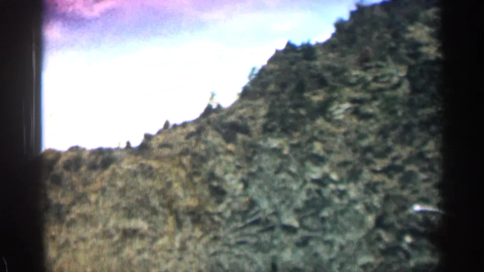 Colorado mountain-road view from 1963 showing a rocky slope, scrub plants, and motion blur from the moving car.