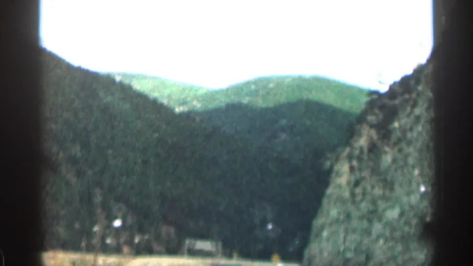 Colorado mountain-pass view with green ridges, a rocky canyon wall, and window framing from the passenger viewpoint.