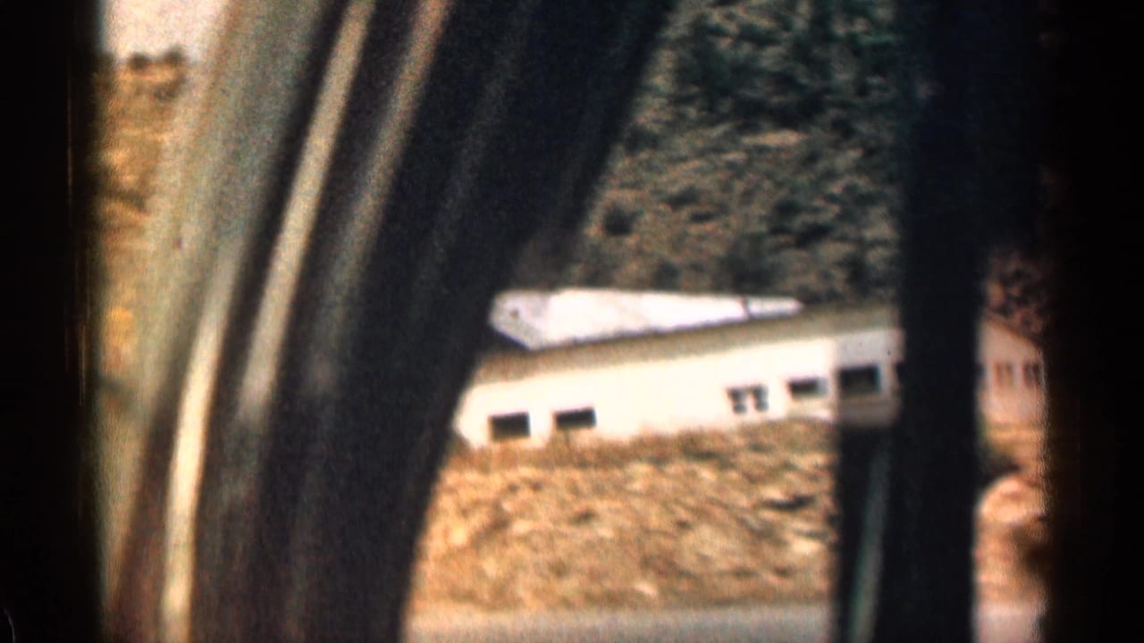 A passing 1963 Colorado mountain-road view frames a white roadside structure through dark car-window pillars and motion blur.