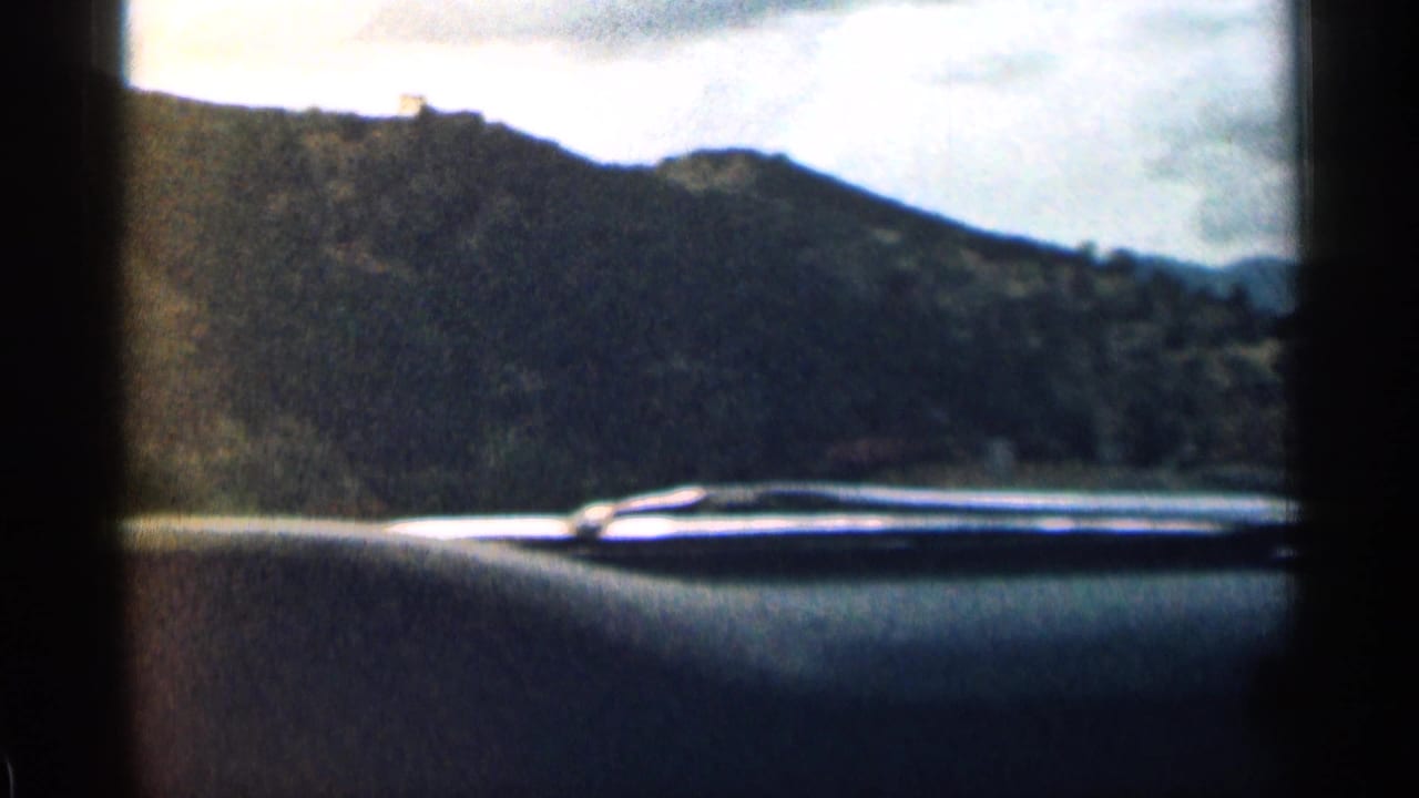 Dark dashboard foreground with a mountain ridge and bright sky seen through the windshield.