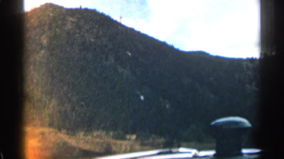 Interior car view in Colorado, showing the dashboard foreground and a shadowed mountain slope under a bright sky.