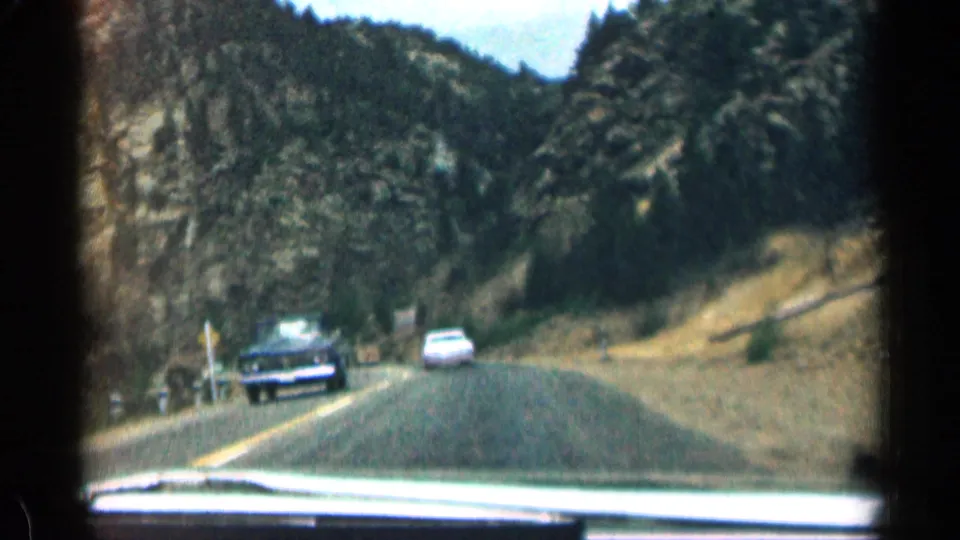 1963 Colorado road-trip frame showing oncoming cars on a two-lane mountain road, viewed through the windshield.