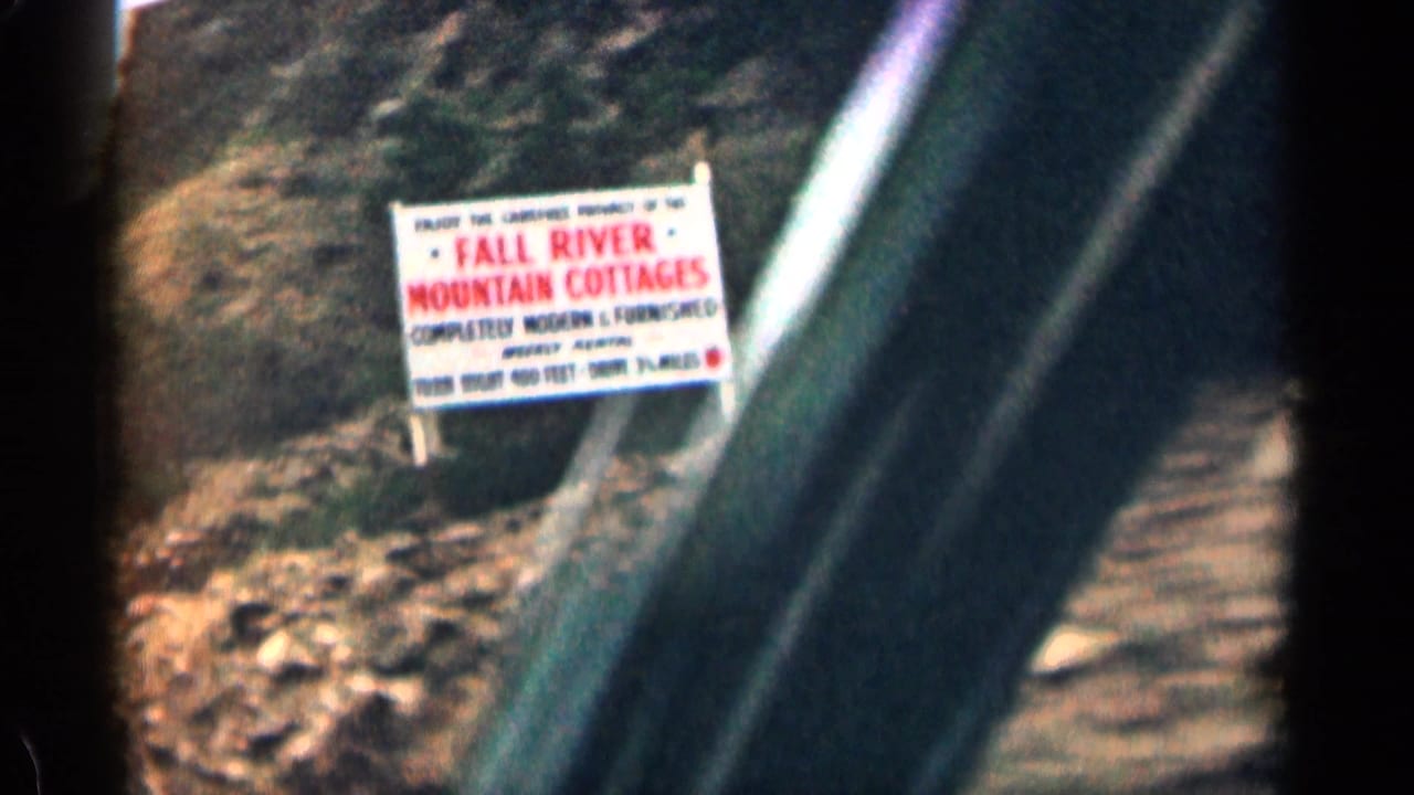 Readable Fall River Mountain Camp sign beside a rocky road viewed from a car.