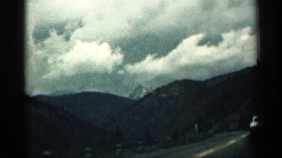 1963 Colorado home-movie view of a winding mountain road, dark hills, and bright cloud banks seen from a moving vehicle.