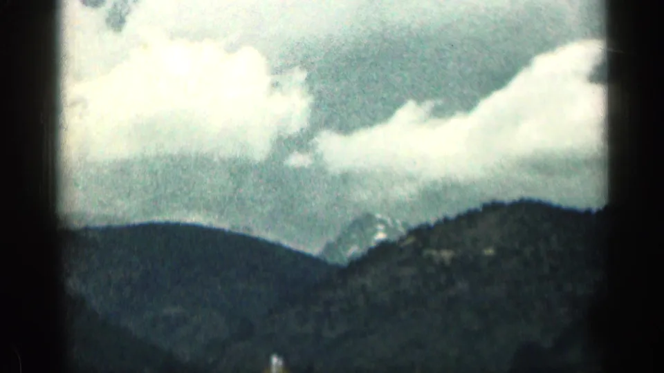 1963 Colorado mountain-driving footage showing distant ridges, bright clouds, and darkened 8mm frame borders from a moving vehicle.