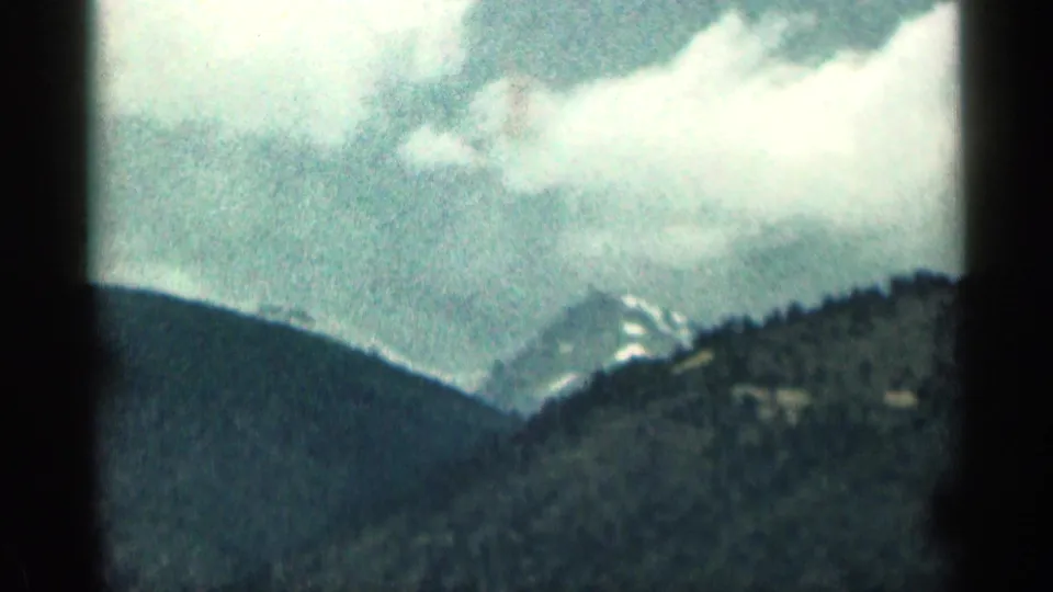 Colorado mountain view from a 1963 home movie, with layered ridges, cloud cover, and a distant snowy peak.