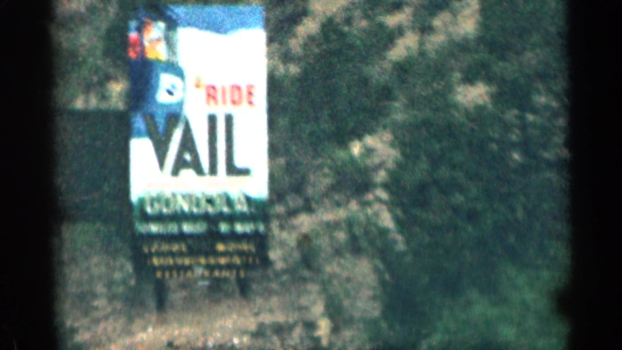 1963 Colorado home-movie frame showing a roadside Ride Vail gondola billboard against trees and a sloped hillside.