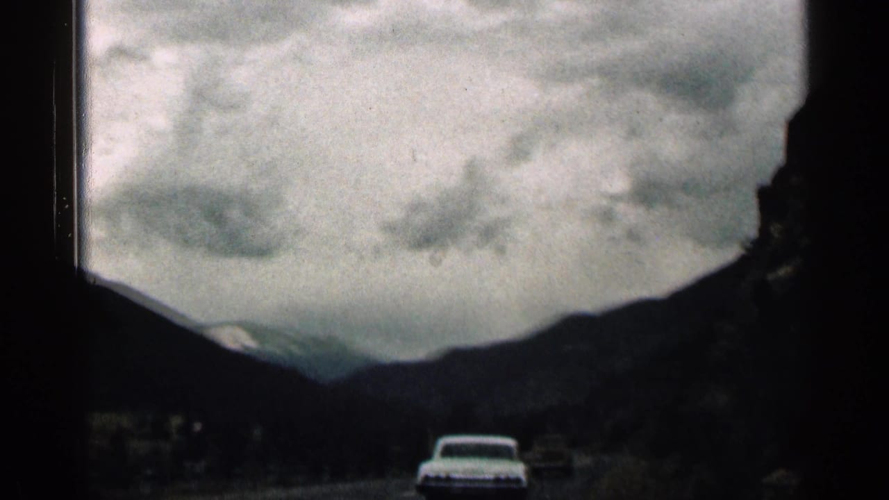White car ahead on a dark mountain road beneath heavy clouds.