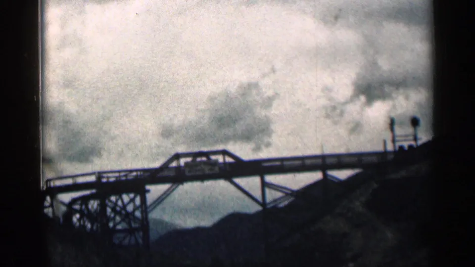 Steel truss bridge with a small sign, cloudy sky, and mountain silhouette in a 1963 Colorado roadside view.