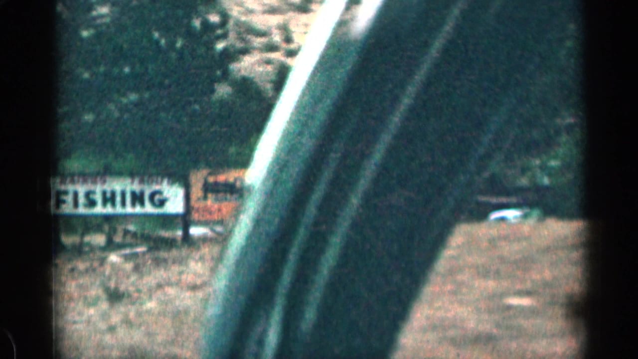 1963 Colorado roadside frame with a large FISHING sign, another sign nearby, parked cars, and the vehicle frame crossing the view.