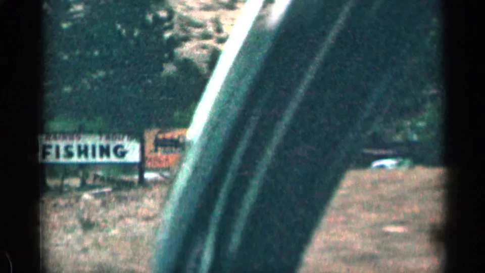 1963 Colorado roadside frame with a large FISHING sign, another sign nearby, parked cars, and the vehicle frame crossing the view.