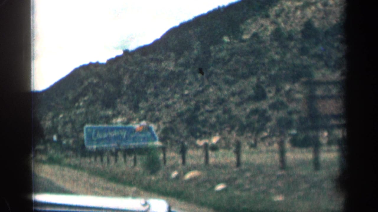 Roadside billboard beside a rocky hillside, seen through a car window.