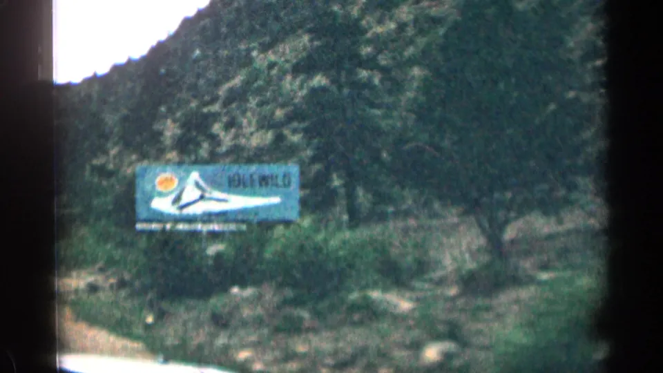 1963 Colorado home-movie frame showing an Idlewild billboard in a rocky roadside setting.