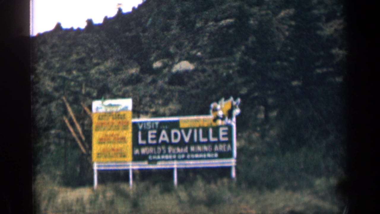 Visit Leadville billboard beside a rocky hillside with a yellow sign panel nearby.