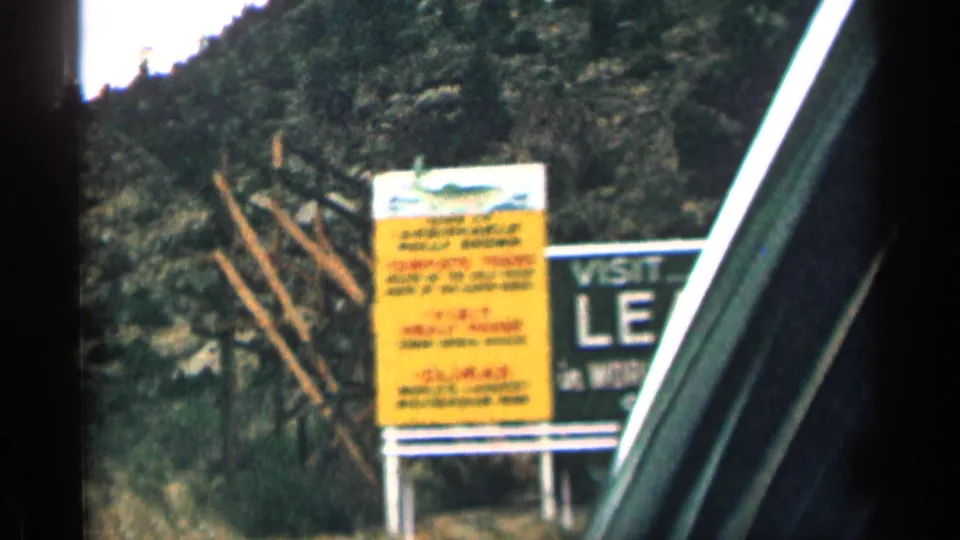 Closer car-window view of a yellow roadside panel and the edge of the Visit Leadville billboard, with the vehicle frame cutting through the scene.