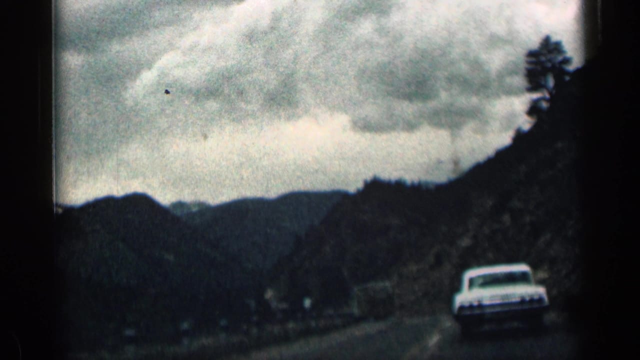 1963 Colorado 8mm frame of a white car ahead on a winding mountain road under an overcast sky.
