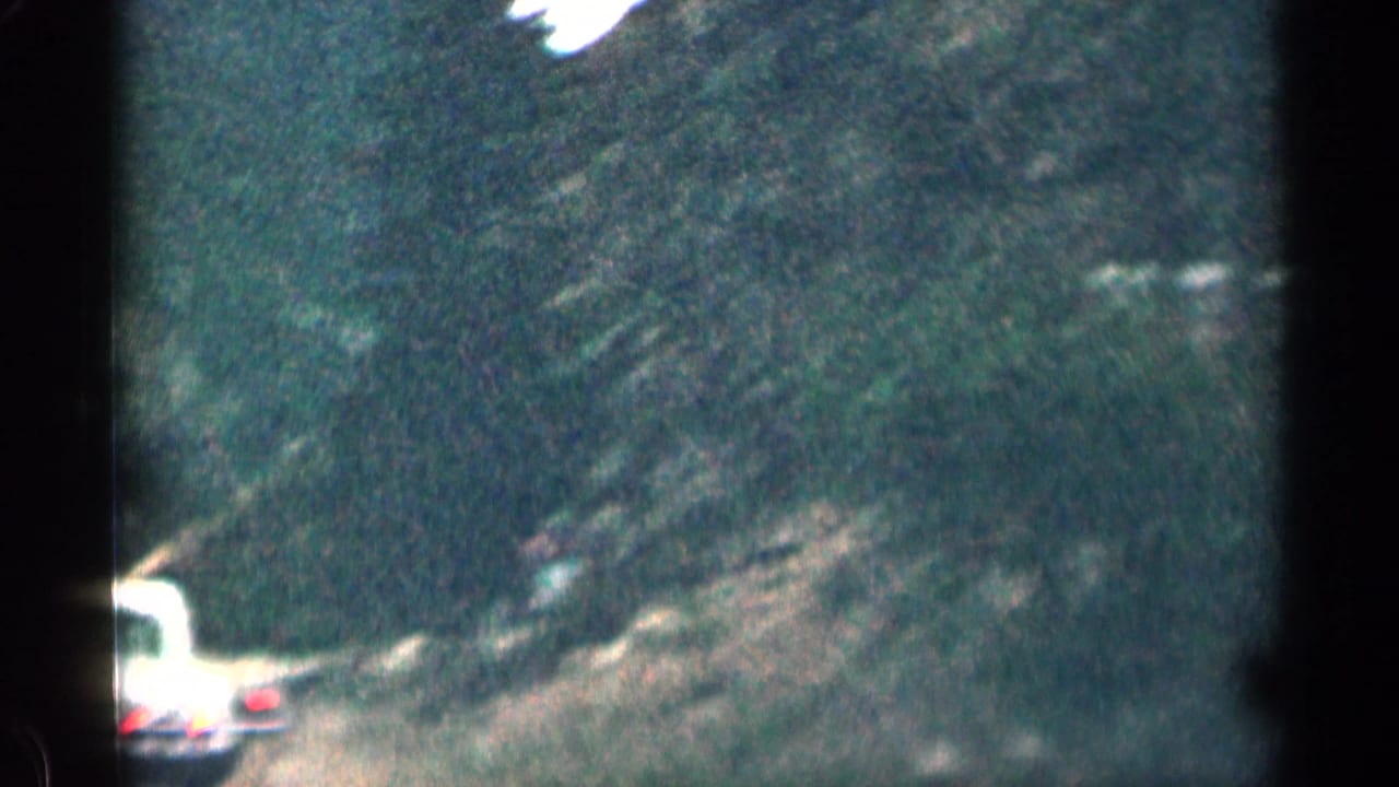 1963 Colorado 8mm frame showing a classic car ahead on a forested mountain road, with soft focus and dark film edges.