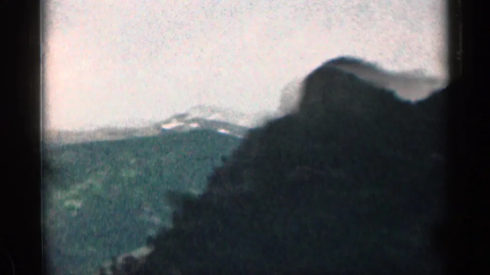 1963 Colorado mountain view with a dark foreground hillside, green ridges, pale sky, and soft 8mm color rendering.