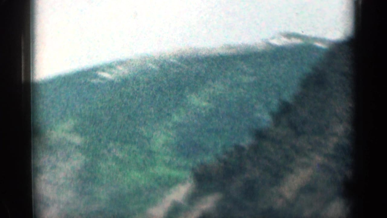 1963 Colorado 8mm frame showing a soft, grainy mountain slope with dark foreground blur and pale sky.