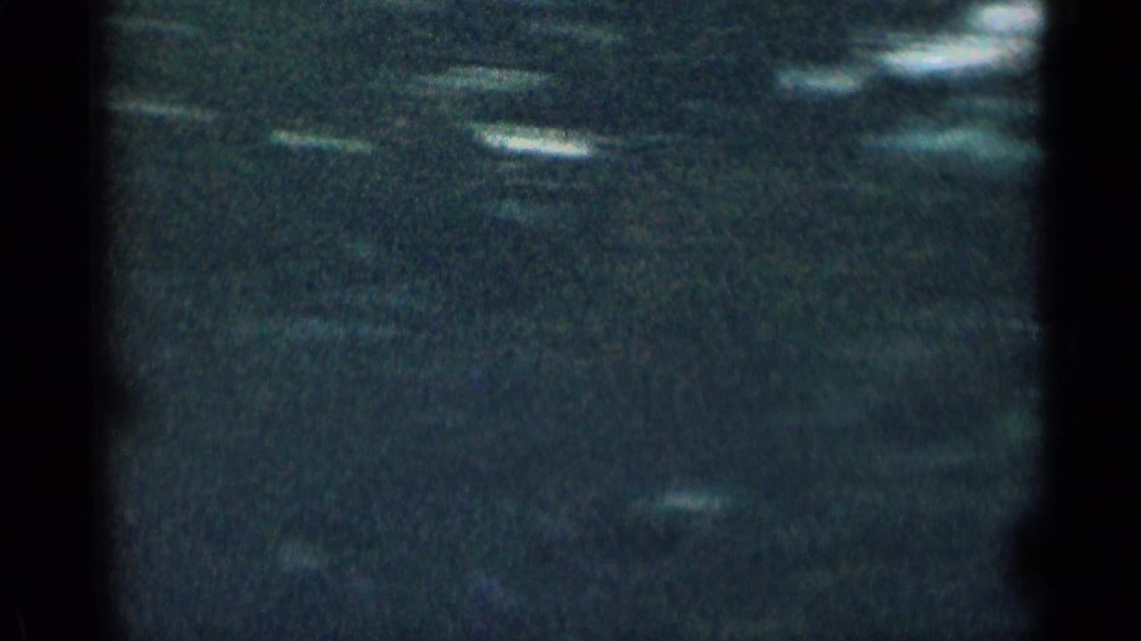 Very dark 8mm frame from the Colorado mountain clip, with faint pale streaks and obscured landscape texture.