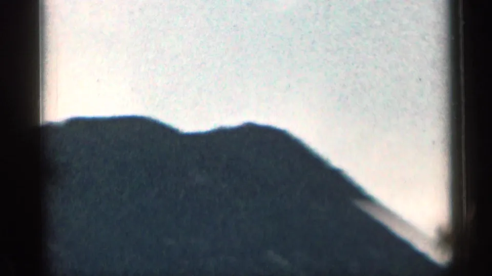 1963 Colorado 8mm frame with a dark mountain ridge profile set against a bright, washed pale sky.