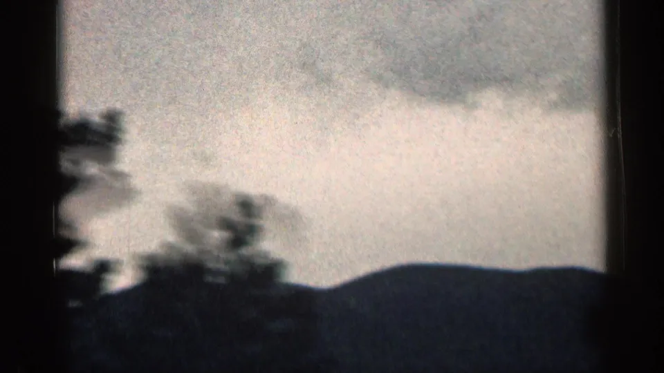 1963 Colorado 8mm frame showing a distant ridge, dark trees in the foreground, and layered cloud cover.