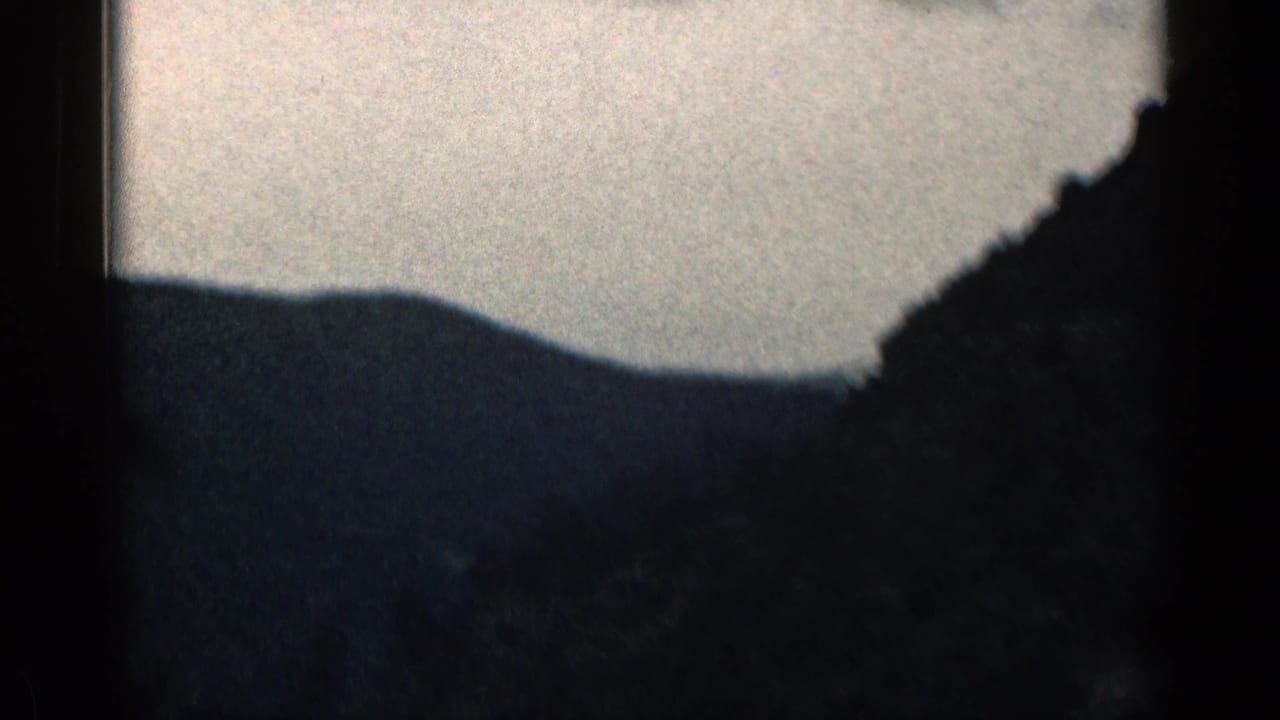 Dark mountain silhouette beneath a bright sky, seen through a film frame edge.