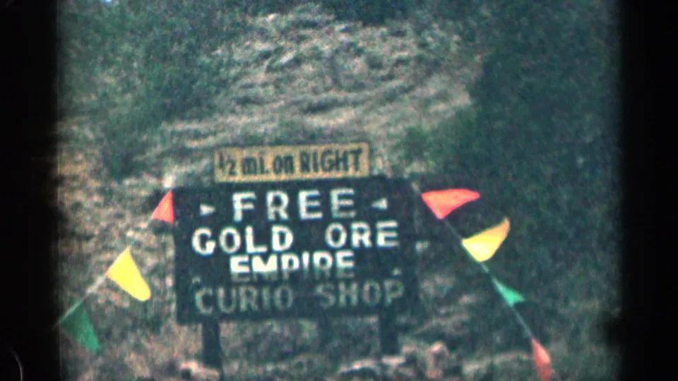1963 Colorado roadside sign advertising free gold ore and an Empire curio shop, flanked by colorful small flags.