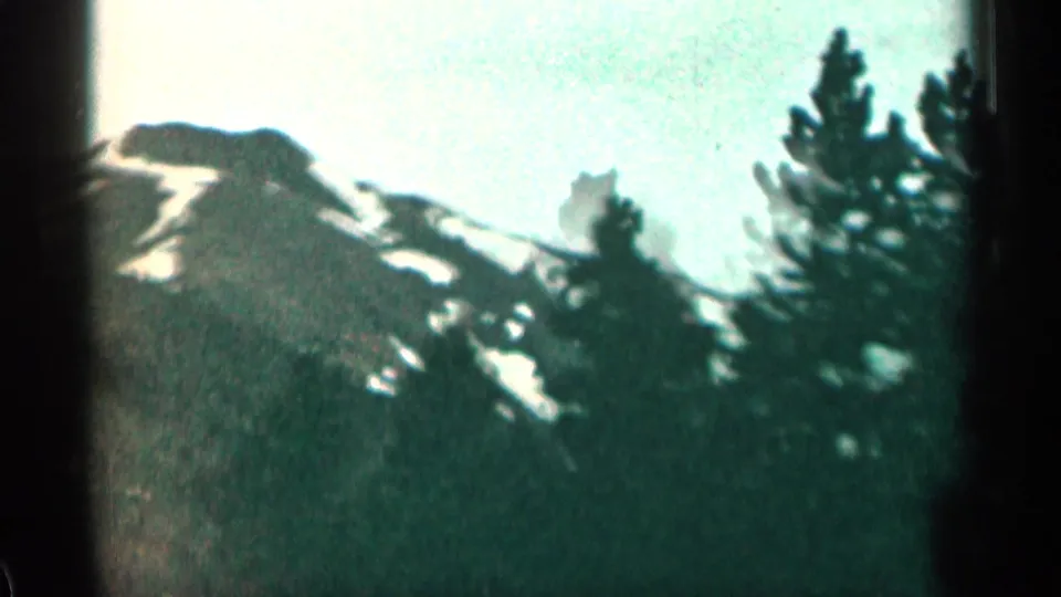 1963 Colorado 8mm frame showing a snow-streaked mountain slope with evergreen trees and soft film focus.