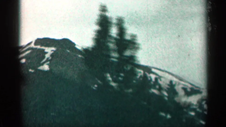 1963 Colorado mountain footage with dark evergreens, snow on the ridge, and visible handheld motion blur.