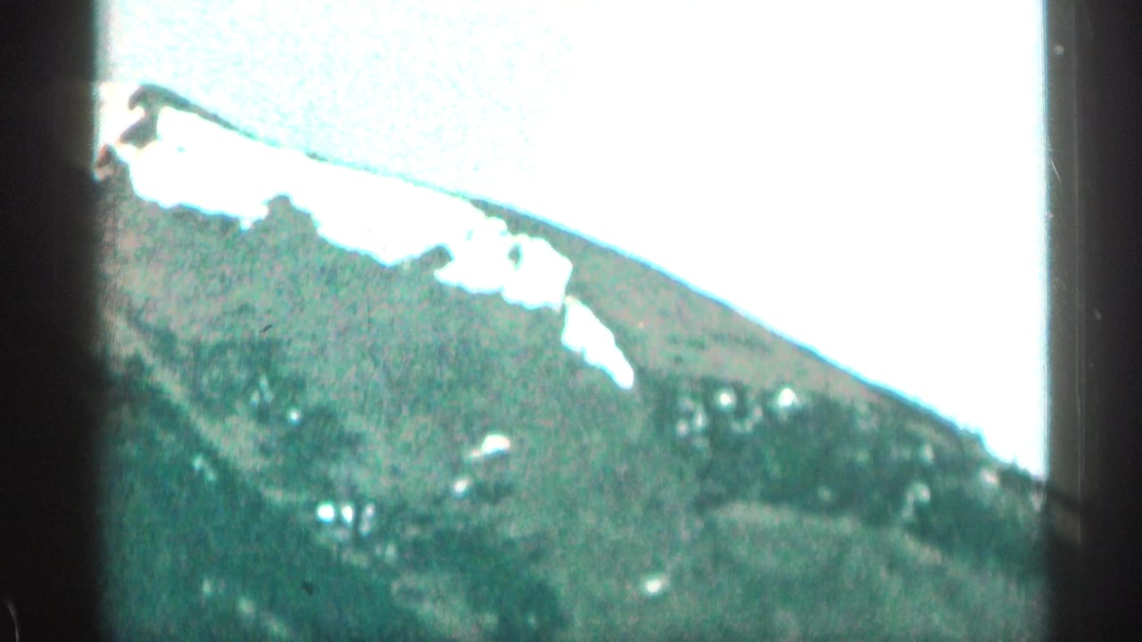 Snow-streaked mountain slope beneath a bright pale sky, seen through soft 8mm framing.