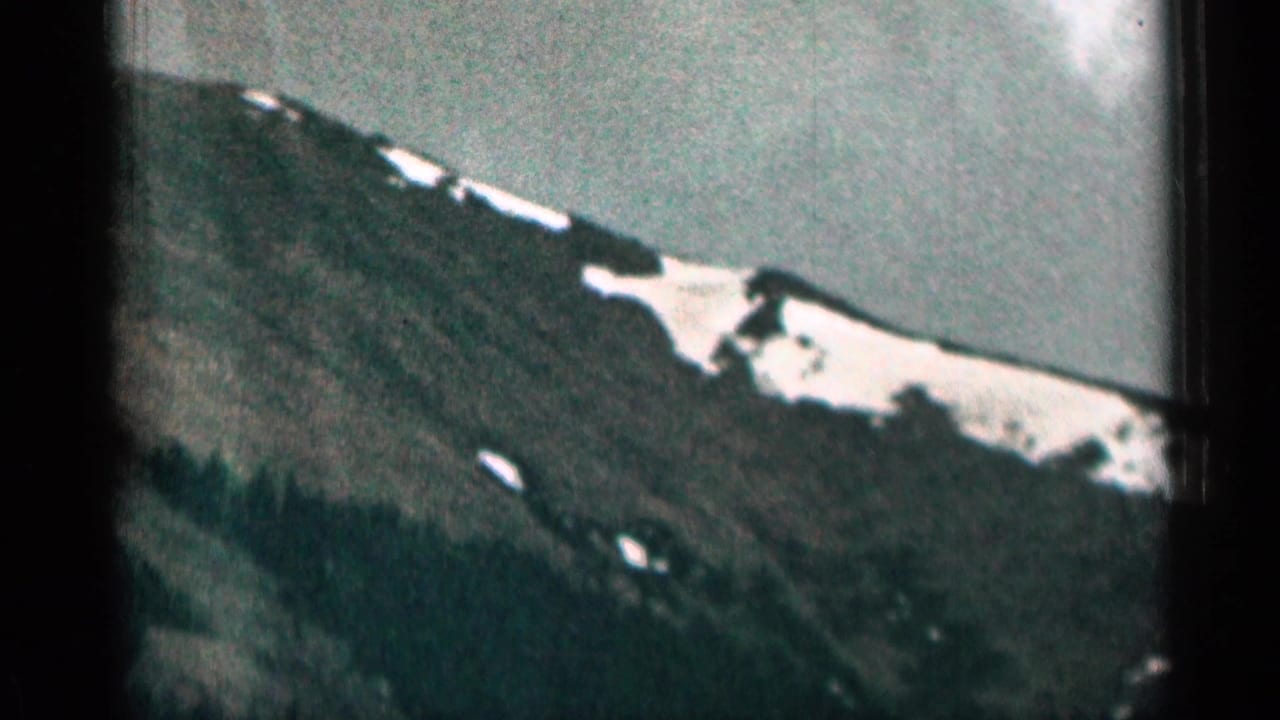 1963 Colorado 8mm view of a forested mountain ridge with irregular snow patches and visible film-frame borders.